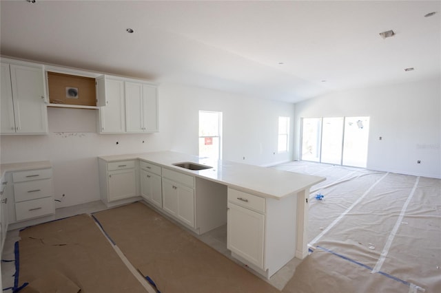 kitchen with a peninsula, a sink, visible vents, vaulted ceiling, and open floor plan