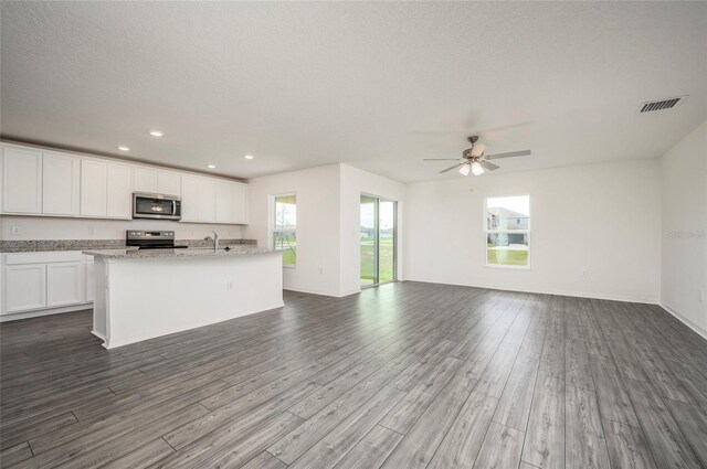 kitchen with appliances with stainless steel finishes, ceiling fan, a kitchen island with sink, hardwood / wood-style floors, and white cabinetry