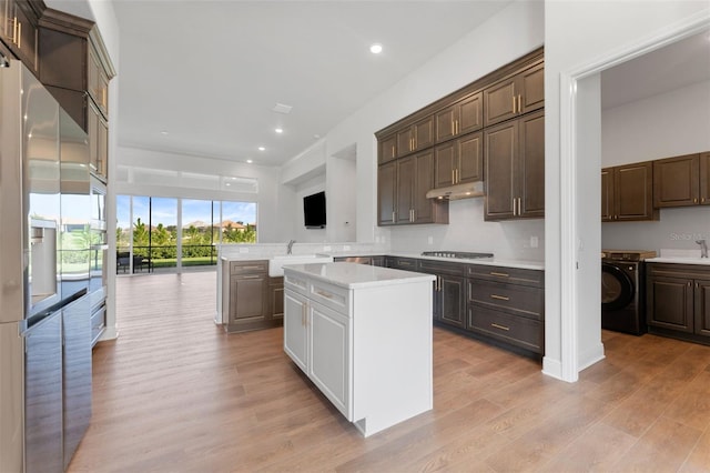 kitchen featuring dark brown cabinetry, washer / clothes dryer, kitchen peninsula, light hardwood / wood-style floors, and a kitchen island