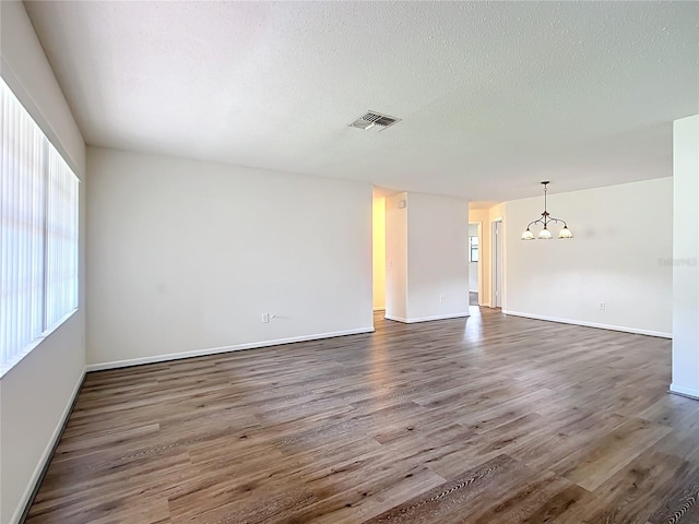 unfurnished room with a textured ceiling, dark hardwood / wood-style flooring, and an inviting chandelier