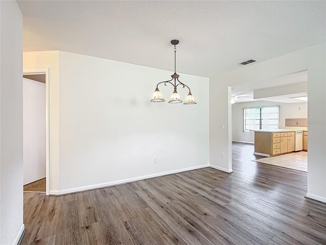 unfurnished dining area with light hardwood / wood-style floors, a textured ceiling, and a notable chandelier