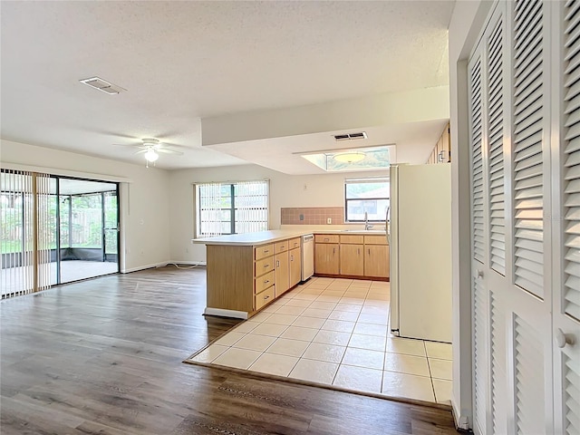 kitchen with light brown cabinets, sink, stainless steel dishwasher, white fridge, and kitchen peninsula