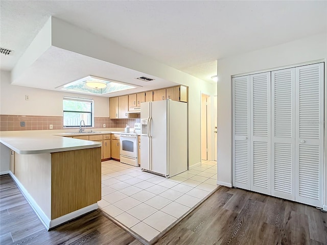 kitchen with white appliances, sink, decorative backsplash, light hardwood / wood-style floors, and kitchen peninsula