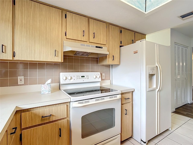 kitchen with decorative backsplash, white appliances, light tile patterned floors, and a skylight