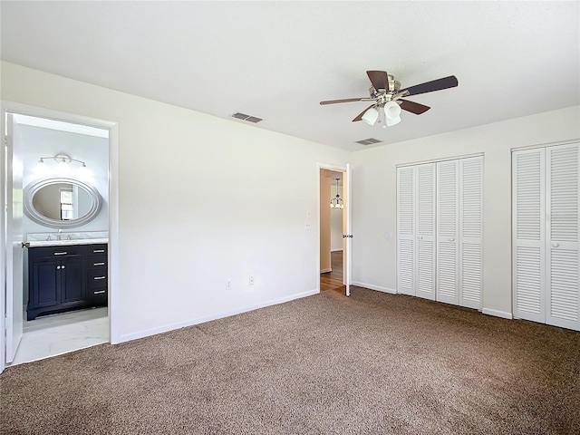 unfurnished bedroom featuring light carpet, two closets, ensuite bath, and ceiling fan