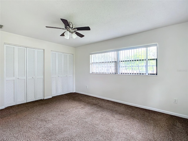 unfurnished bedroom featuring ceiling fan, carpet floors, a textured ceiling, and multiple closets