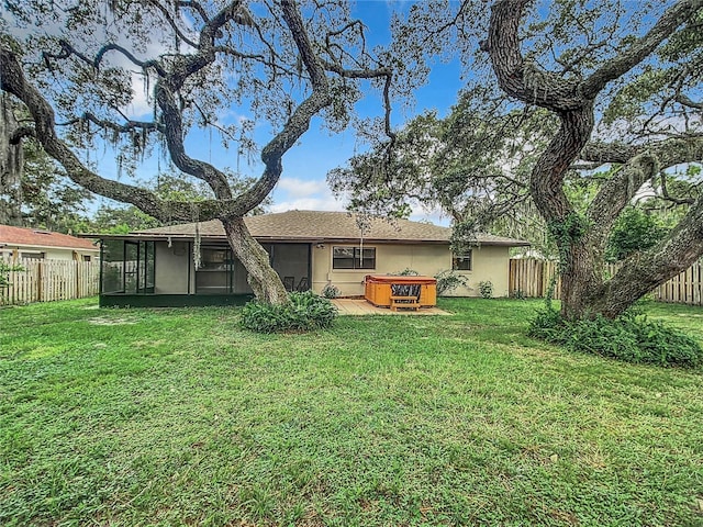 rear view of property featuring a sunroom, a yard, and a hot tub