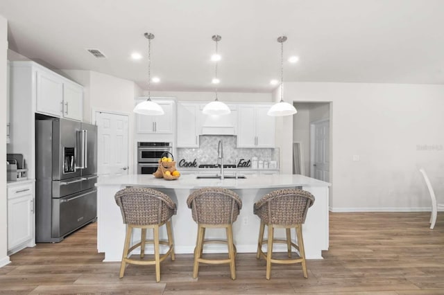 kitchen featuring white cabinetry, an island with sink, decorative light fixtures, and appliances with stainless steel finishes