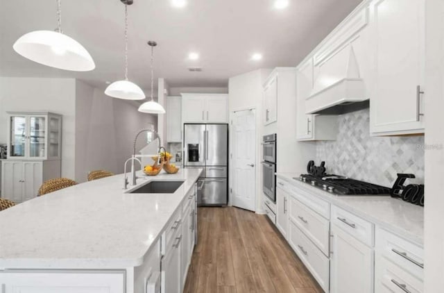 kitchen featuring appliances with stainless steel finishes, a large island with sink, decorative light fixtures, hardwood / wood-style flooring, and white cabinets