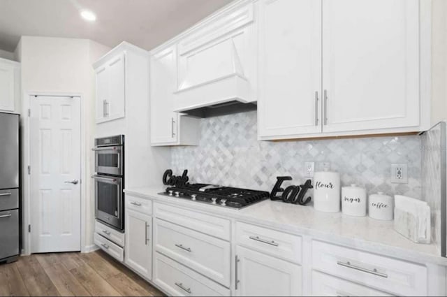 kitchen with premium range hood, light stone countertops, light wood-type flooring, appliances with stainless steel finishes, and white cabinetry