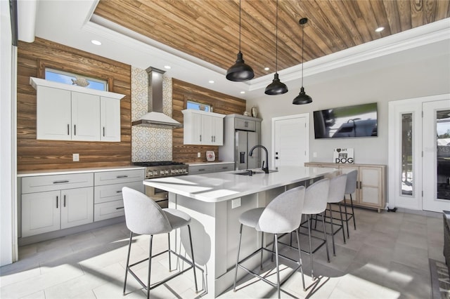 kitchen with a center island with sink, wall chimney range hood, sink, tasteful backsplash, and stainless steel appliances