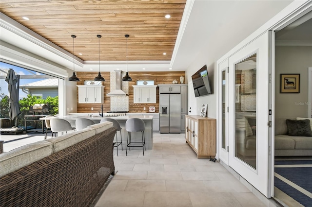 kitchen featuring tasteful backsplash, a breakfast bar, wall chimney range hood, decorative light fixtures, and stainless steel fridge with ice dispenser