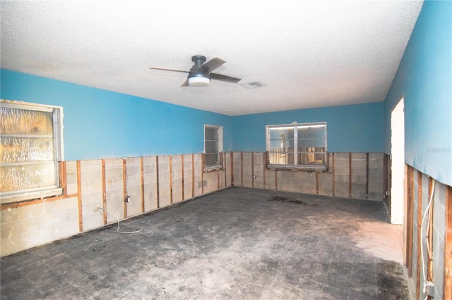 unfurnished room with concrete block wall, ceiling fan, visible vents, and a textured ceiling