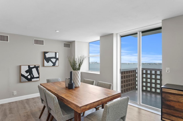 dining area with hardwood / wood-style floors, a water view, and expansive windows