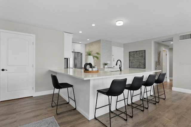 kitchen featuring a breakfast bar area, stainless steel fridge, white cabinets, and hardwood / wood-style flooring