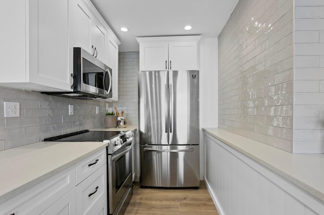 kitchen with white cabinetry, light stone countertops, stainless steel appliances, light hardwood / wood-style flooring, and backsplash