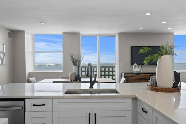 kitchen with dishwasher, sink, light stone counters, a water view, and white cabinets