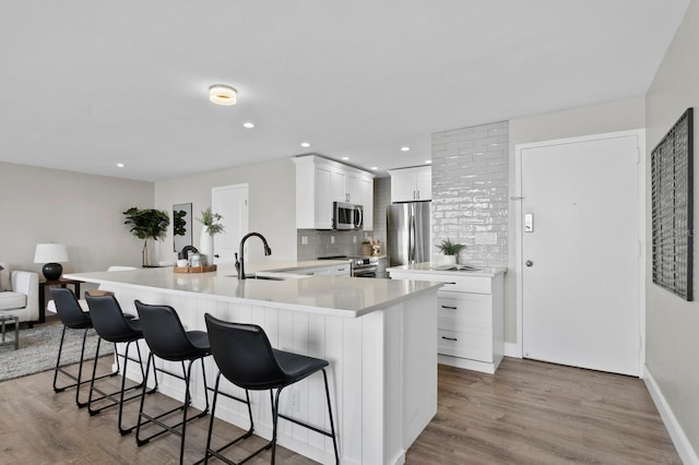 kitchen with backsplash, light hardwood / wood-style floors, a kitchen bar, white cabinetry, and stainless steel appliances