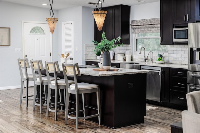 kitchen with decorative light fixtures, light hardwood / wood-style flooring, appliances with stainless steel finishes, a kitchen breakfast bar, and a kitchen island