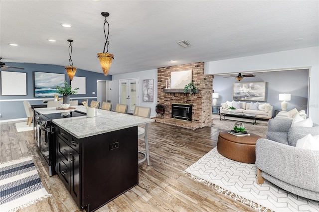 kitchen featuring pendant lighting, an island with sink, a breakfast bar area, light hardwood / wood-style floors, and black electric range