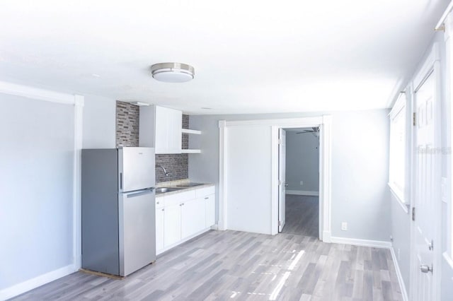 kitchen featuring stainless steel refrigerator, white cabinetry, sink, tasteful backsplash, and light hardwood / wood-style flooring