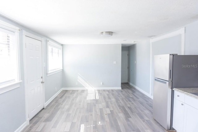 kitchen with white cabinets, a textured ceiling, light wood-type flooring, and stainless steel refrigerator