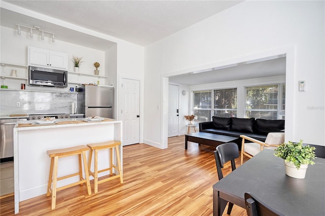 kitchen with a kitchen breakfast bar, tasteful backsplash, light hardwood / wood-style flooring, white cabinets, and appliances with stainless steel finishes