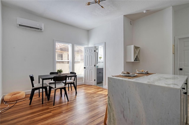 dining space featuring light wood-type flooring, an AC wall unit, and a textured ceiling