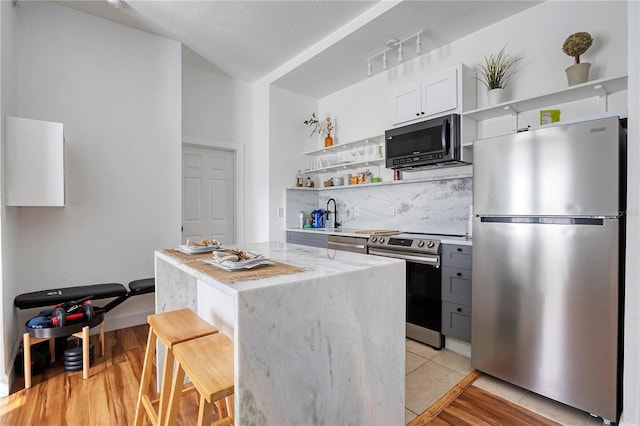 kitchen with white cabinetry, stainless steel appliances, light stone counters, a breakfast bar, and a kitchen island