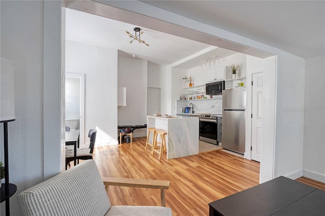 kitchen with white cabinetry, a chandelier, a breakfast bar, appliances with stainless steel finishes, and light wood-type flooring