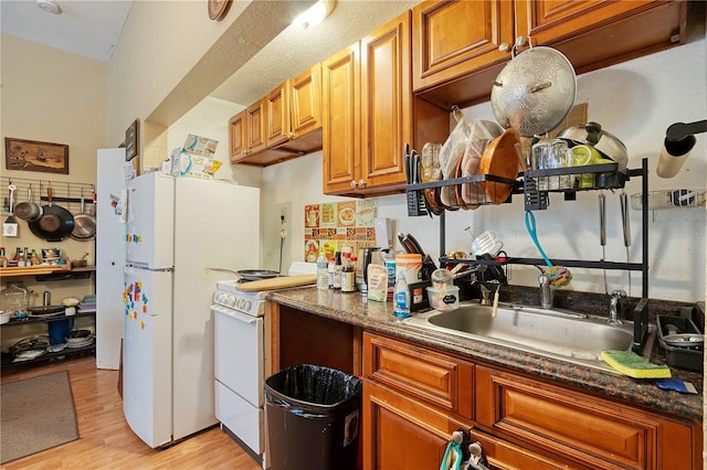 kitchen with white appliances, light hardwood / wood-style floors, dark stone countertops, and sink