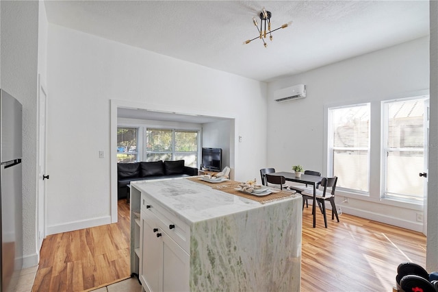 kitchen featuring white cabinets, an AC wall unit, stainless steel fridge, light hardwood / wood-style floors, and a chandelier