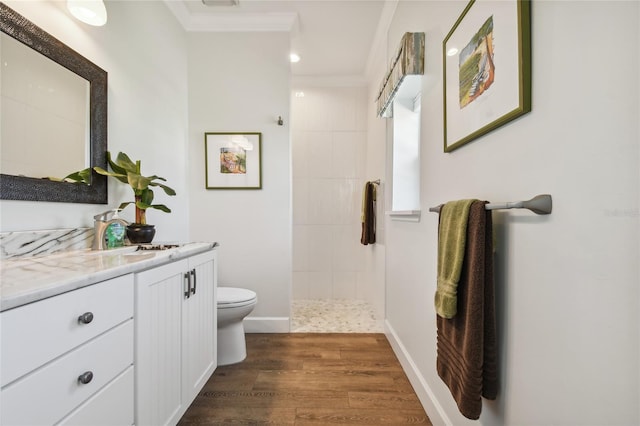 bathroom with a tile shower, wood-type flooring, toilet, vanity, and ornamental molding