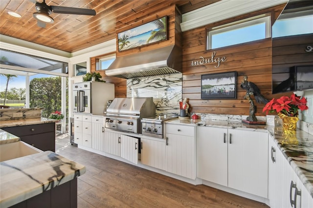 kitchen featuring dark wood-type flooring, wooden walls, wall chimney range hood, wooden ceiling, and white cabinetry