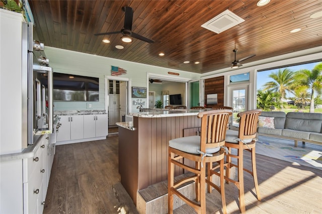 kitchen with kitchen peninsula, dark hardwood / wood-style flooring, wood ceiling, a breakfast bar, and white cabinets