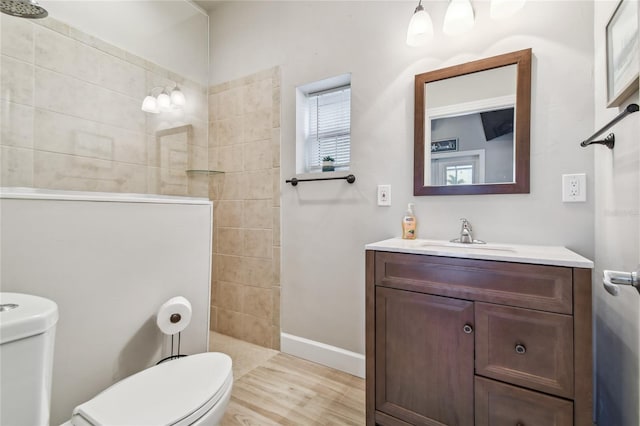 bathroom featuring hardwood / wood-style flooring, vanity, toilet, and tiled shower