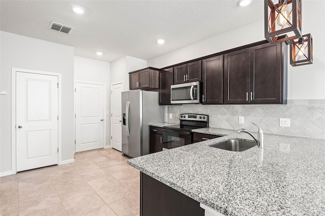 kitchen featuring dark brown cabinetry, sink, light stone counters, decorative backsplash, and appliances with stainless steel finishes