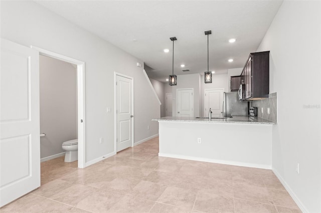 kitchen with dark brown cabinetry, light stone counters, kitchen peninsula, decorative light fixtures, and appliances with stainless steel finishes