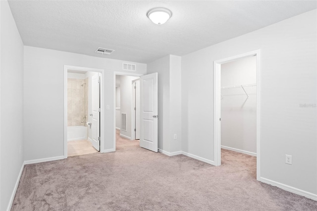 unfurnished bedroom with light carpet, ensuite bath, a spacious closet, a textured ceiling, and a closet