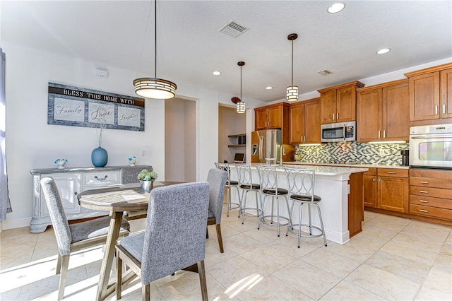 kitchen featuring decorative backsplash, an island with sink, decorative light fixtures, and appliances with stainless steel finishes