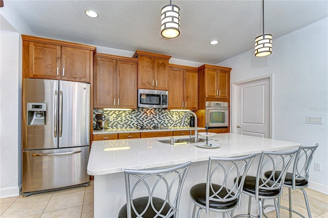 kitchen featuring light stone countertops, appliances with stainless steel finishes, a kitchen island with sink, sink, and decorative light fixtures