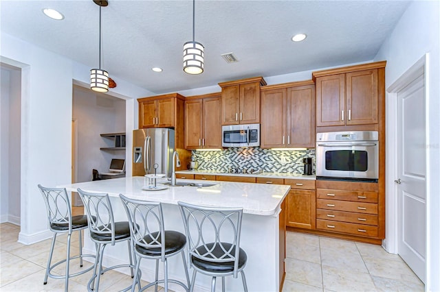 kitchen with sink, stainless steel appliances, a kitchen breakfast bar, decorative light fixtures, and a kitchen island with sink