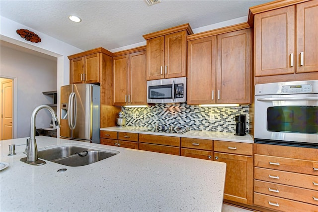 kitchen with backsplash, light stone countertops, sink, and stainless steel appliances