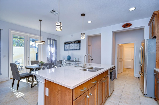 kitchen featuring light stone counters, stainless steel appliances, sink, decorative light fixtures, and an island with sink