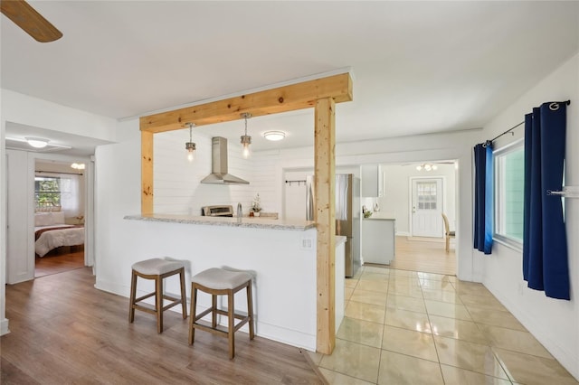 kitchen with pendant lighting, white cabinets, a kitchen breakfast bar, wall chimney range hood, and kitchen peninsula