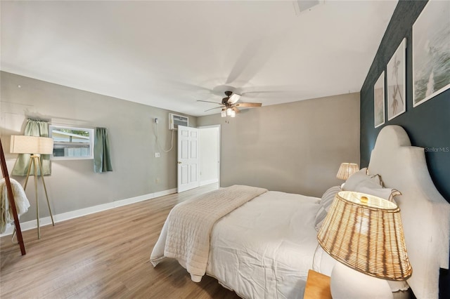 bedroom with a wall unit AC, ceiling fan, and wood-type flooring