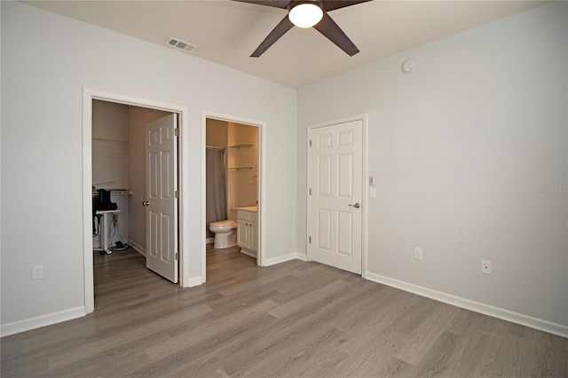 unfurnished bedroom featuring baseboards, visible vents, wood finished floors, a walk in closet, and a closet