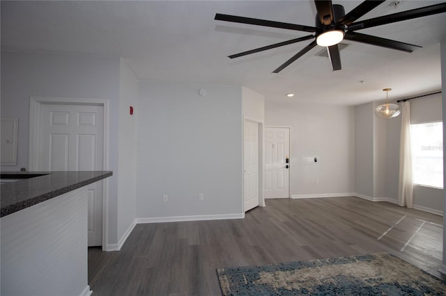 unfurnished living room featuring dark wood-type flooring, ceiling fan, and baseboards