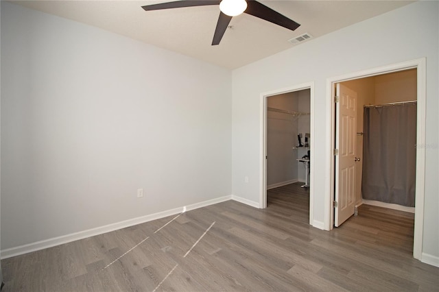 unfurnished bedroom featuring a closet, baseboards, a walk in closet, and wood finished floors