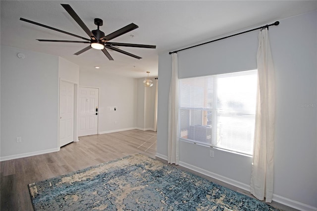 empty room featuring ceiling fan, plenty of natural light, baseboards, and wood finished floors